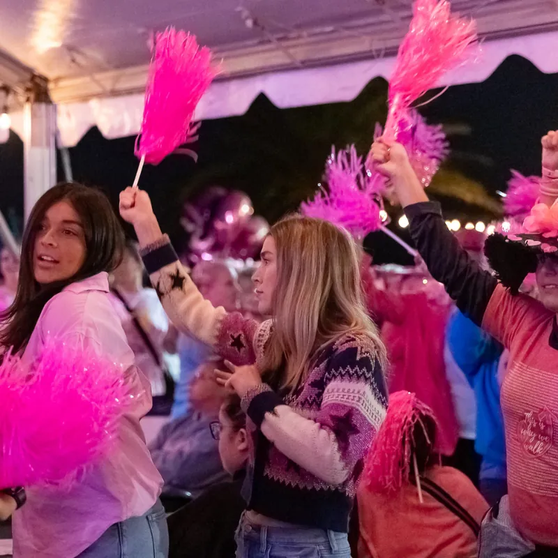 The crowd waving pink pom-poms under the big tent at night.