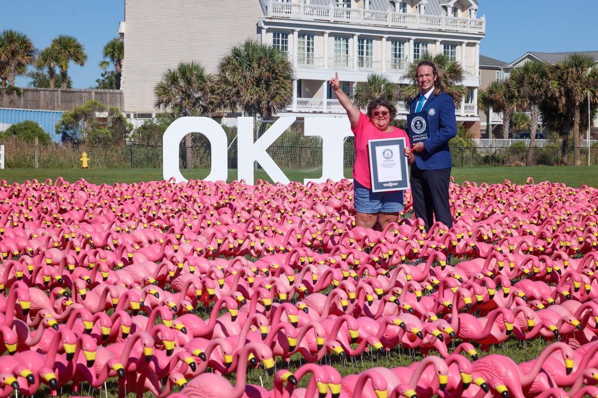 A Pledge the Pink organizer and a Guinness World Records adjudicator holding the record certificate in the flamingo field, in front of the giant OKI letters