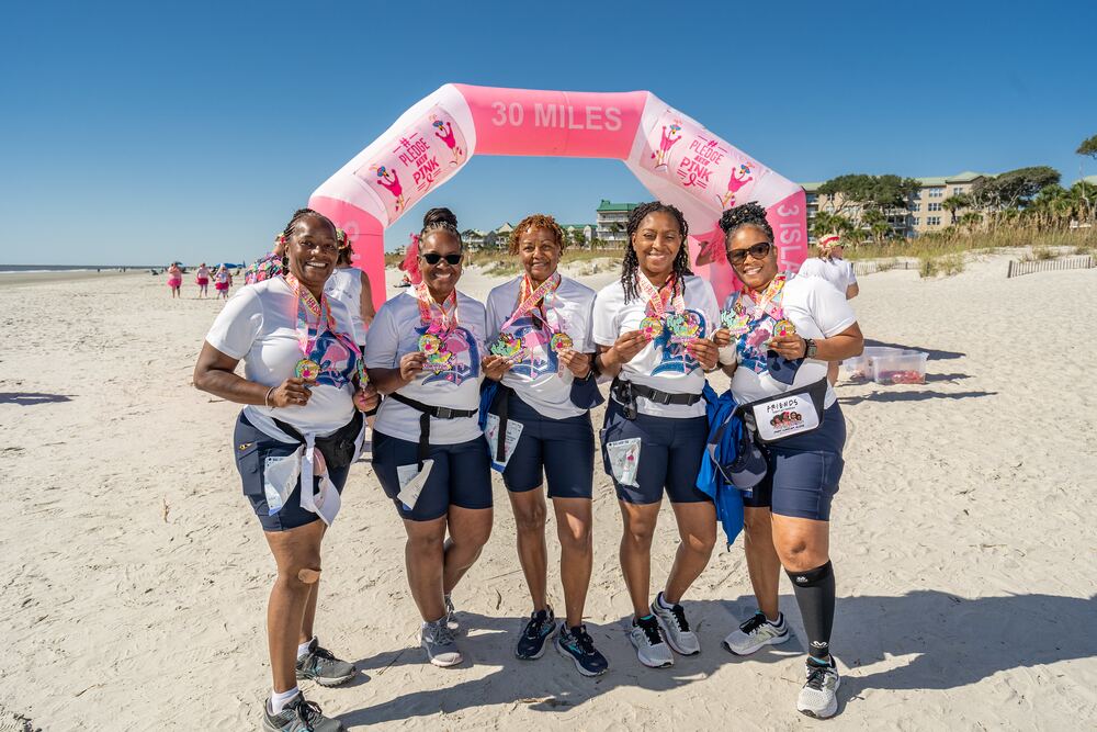 Five women showing off their medals on the beach
