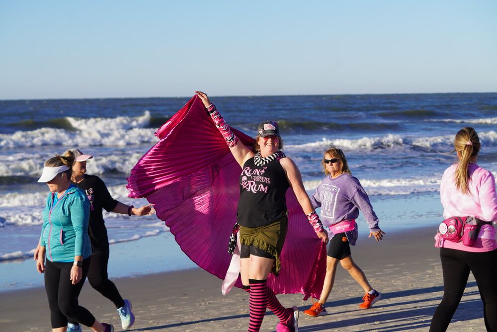 Woman twirling a pink cape on the beach