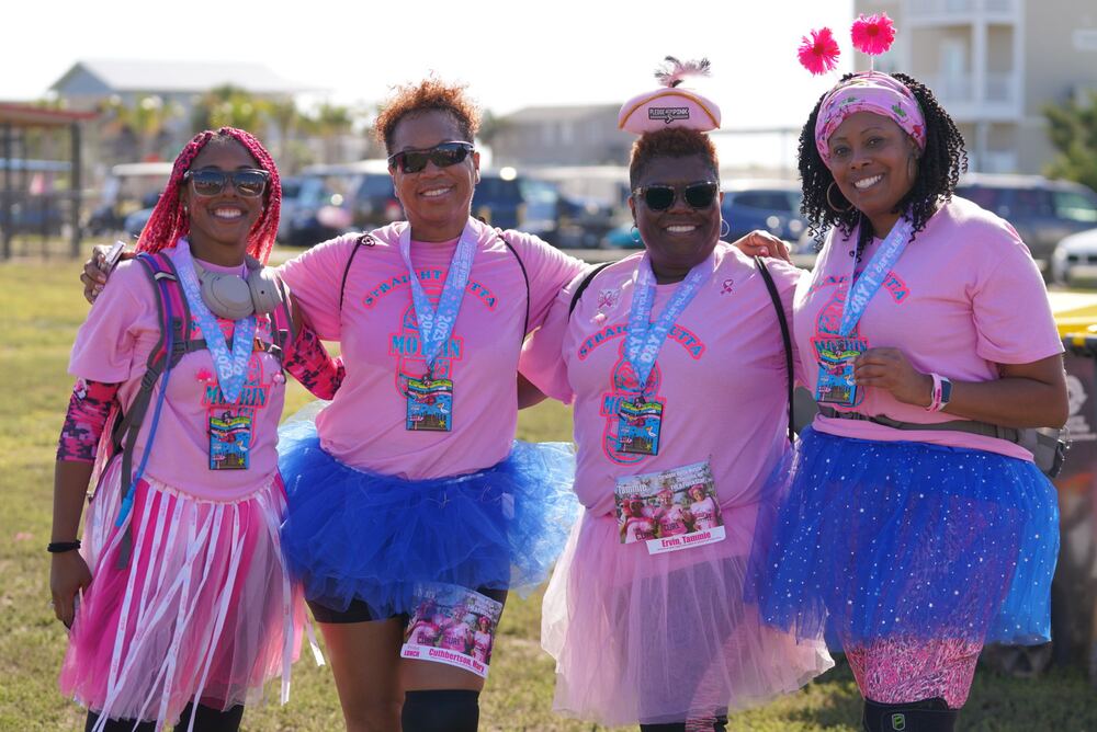 Four women in pink shirts and tutus showing their medals