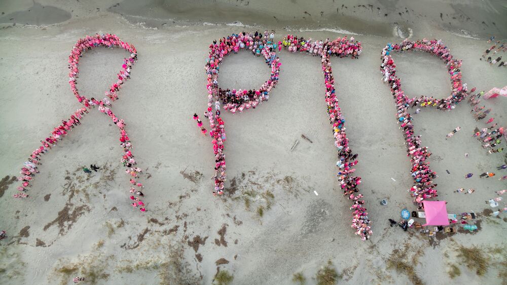 Aerial view of walkers forming a pink ribbon and the letters PTP on the beach