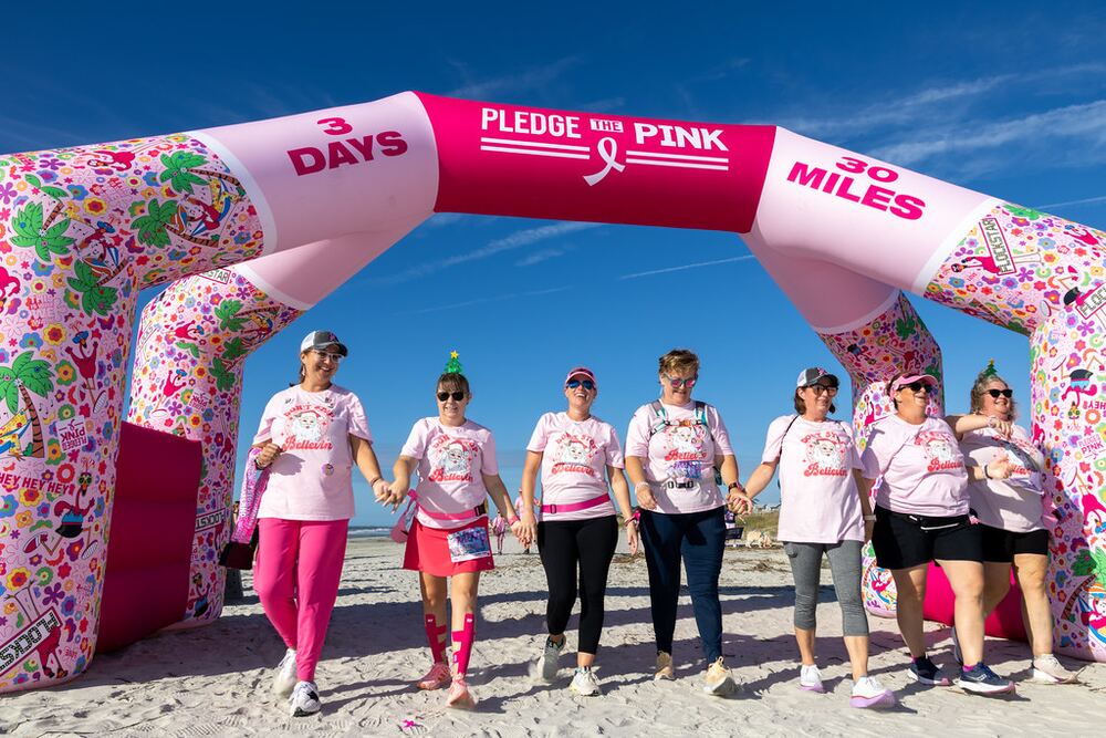 Walkers holding hands under the Pledge the Pink 3 Days 30 Miles arch