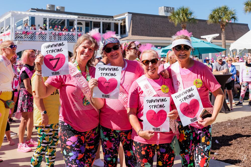 Four women in pink sashes holding Surviving Strong signs