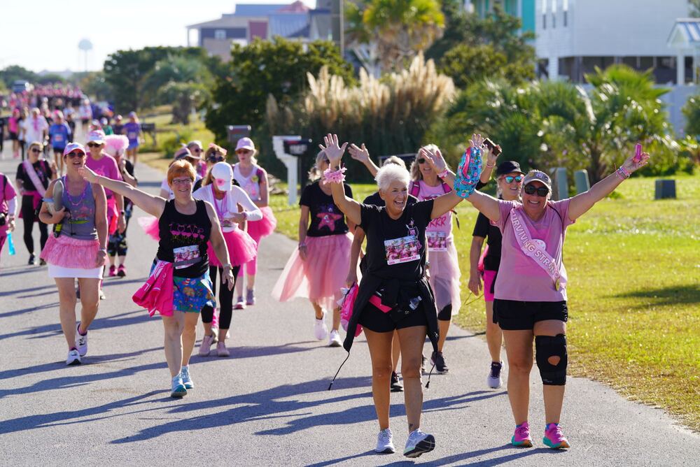 Walkers in tutus and sashes cheering with arms raised on the course
