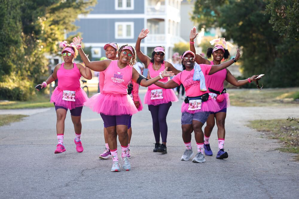 Five walkers in pink tutus waving as they walk down the road