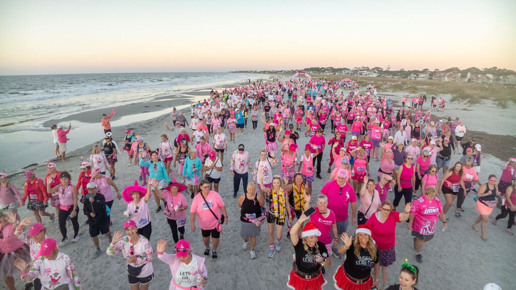 A huge crowd of FlockStars in pink walking along the beach at sunset