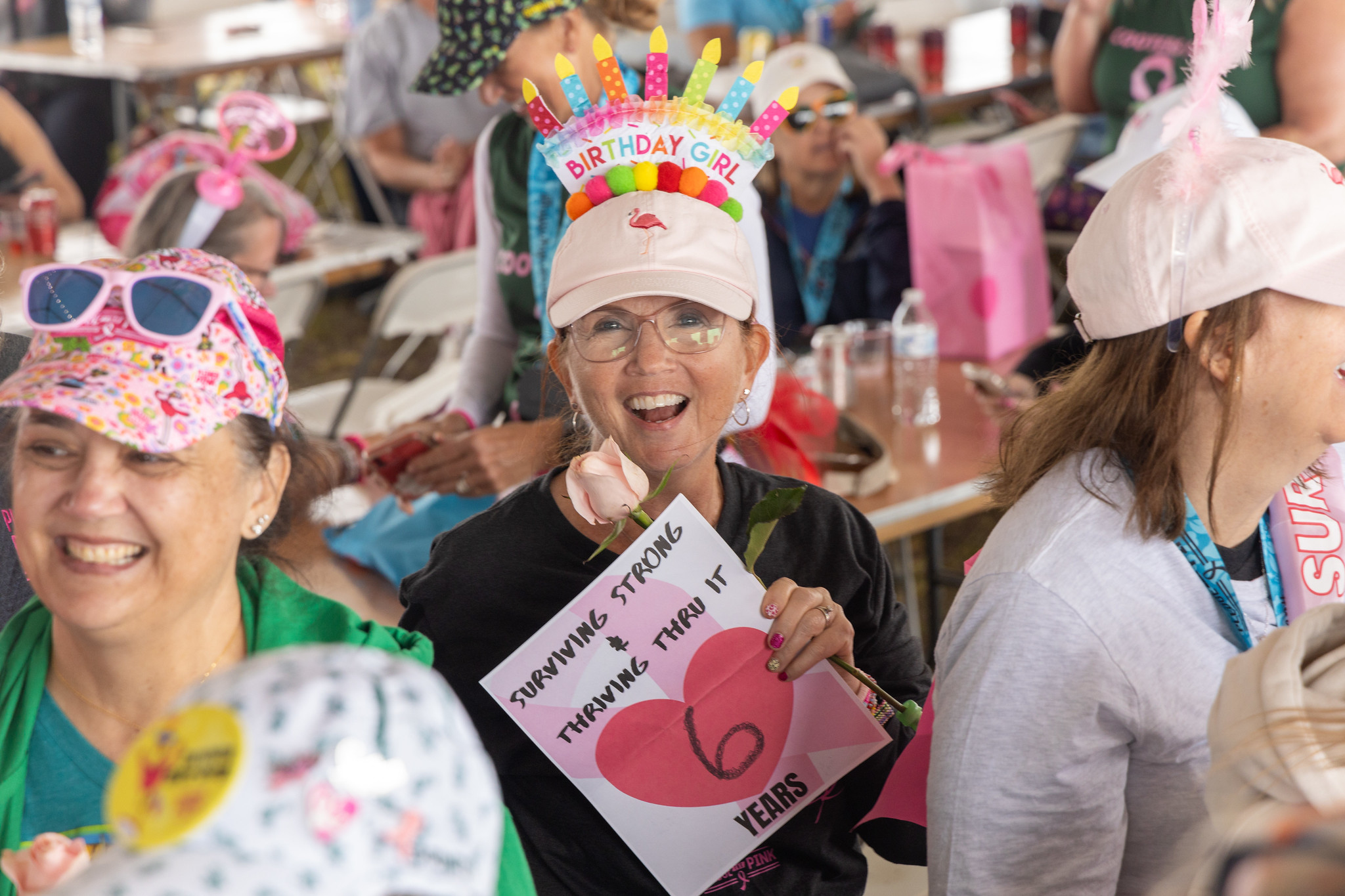 A survivor in a birthday-cake hat holding a Surviving Strong 6 years sign at the luncheon
