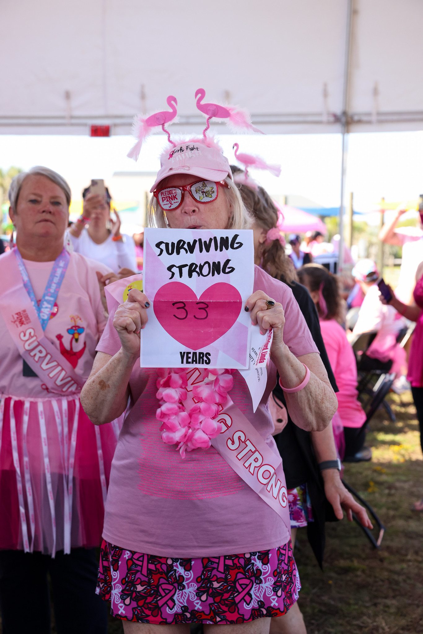 A survivor in flamingo antennae holding a Surviving Strong 33 years sign
