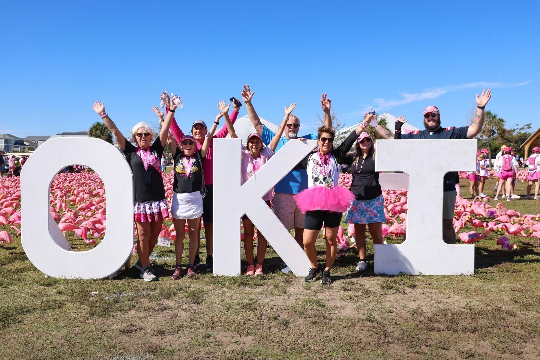 FlockStars cheering in front of the giant OKI letters, surrounded by the flamingo field