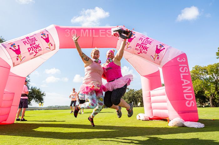 Two women jumping for joy under the Pledge the Pink finish arch