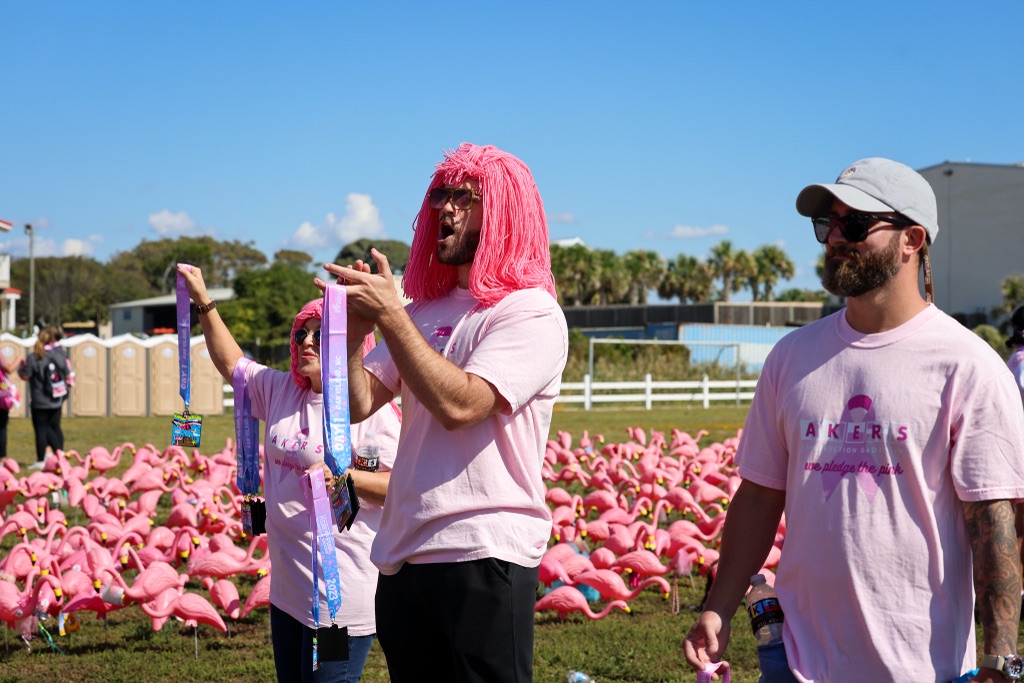 A FlockStar in a pink wig cheering in front of thousands of plastic flamingos