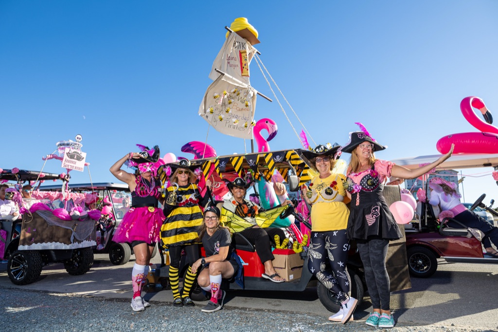 A team in pirate and bumblebee costumes posing with their decorated golf cart