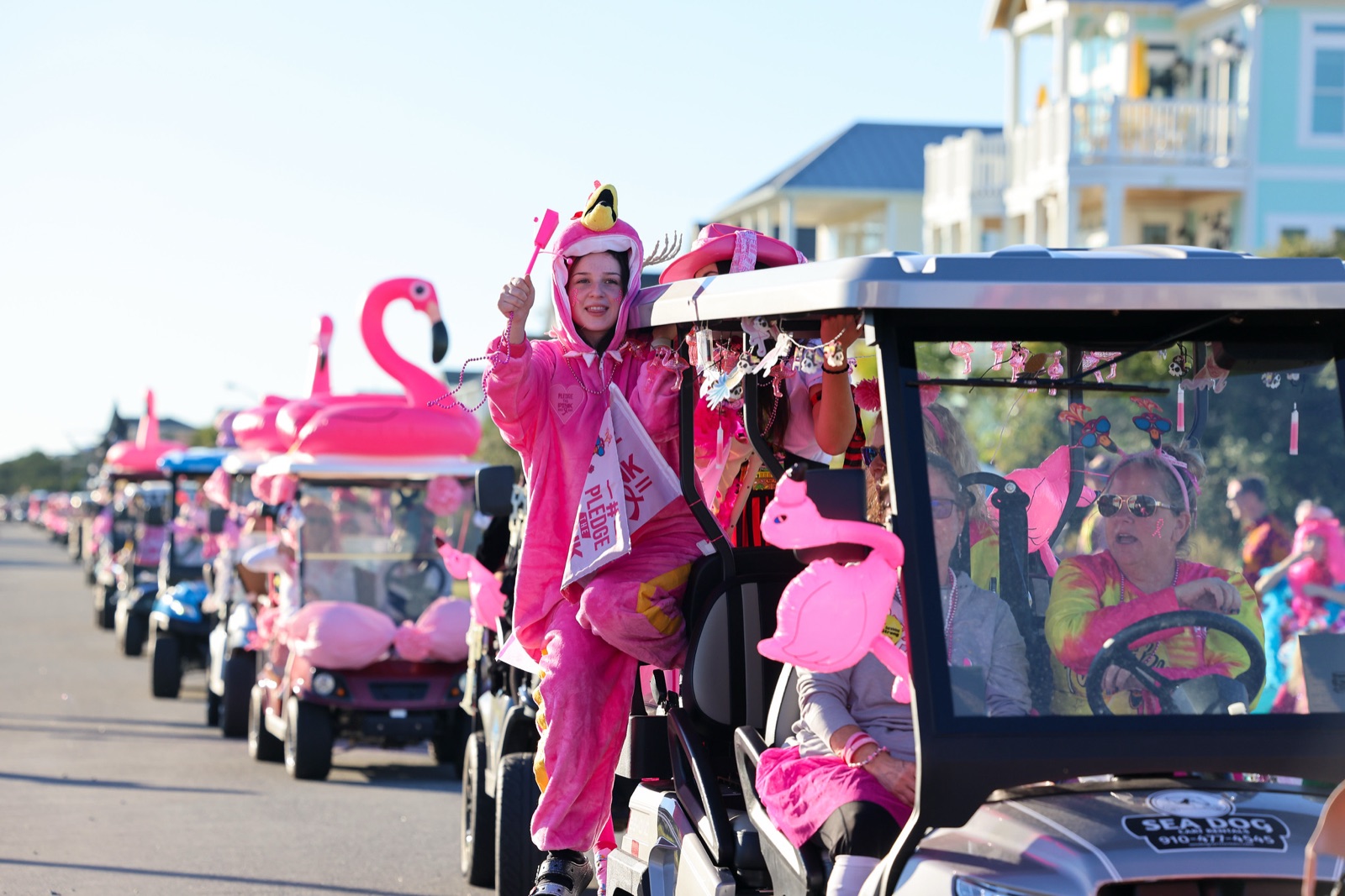 A line of golf carts covered in flamingos rolling down an Oak Island street