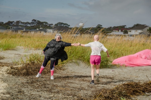 A volunteer in a black poncho and pink socks high-fives a registrant in pink shorts on a sandy path through the dunes.