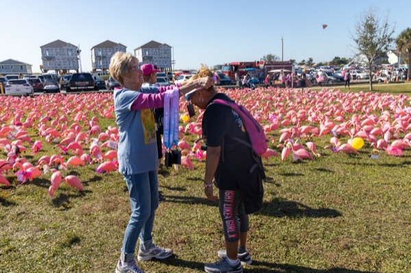 A volunteer hangs a medal around a finisher’s neck on a lawn filled with pink flamingos.